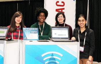 Four Materials Voice volunteers pose behind two laptops at the MRS Meeting